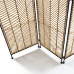 Folding room divider with a thin black frame and weaved wicker centers in a geometrical pattern, featuring three panels.