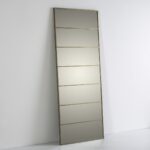 Tall rectangular floor-standing mirror with glass panels and a gold metal frame, leaning against a wall.