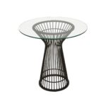 Round NIXON dining table with a clear glass top and matte black stainless steel geometric base, exuding modern retro charm.
