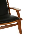 JOEY Chair with sculpted teak wood frame, plain black leather upholstery, stud detail, and mid-century modern architectural design.