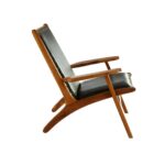 JOEY Chair with sculpted teak wood frame, plain black leather upholstery, stud detail, and mid-century modern architectural design.