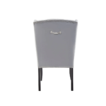 Grey velvet dining chair with a button-tufted wingback, padded seat, stud trim detailing, and curved black wood legs.