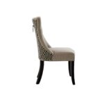 Grey linen dining chair with button tufting, black wooden legs, and a decorative metal knocker on the back.