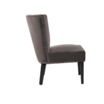 Dark mink velvet dining chair with a wingback design, deep-cushioned seat, black wood legs, and silver stud detailing.