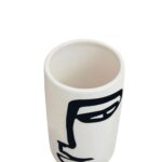 Small white ceramic vase with an abstract black face sketch, featuring a cylindrical shape and minimalist design.