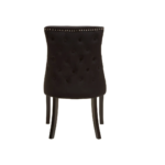 Black velvet dining chair with button-tufted backrest, warm metallic stud detailing, and dark wooden legs.