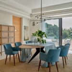 Elegant peacock blue velvet armchair with curved backrest, padded seat, and wooden legs with metallic inserts, designed for modern interiors.