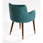 Elegant peacock blue velvet armchair with curved backrest, padded seat, and wooden legs with metallic inserts, designed for modern interiors.