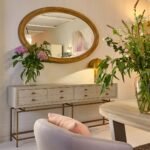 Large oval wall mirror with natural wood frame, styled for luxury interiors such as entrance halls or living rooms.