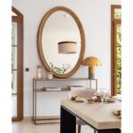Large oval wall mirror with natural wood frame, styled for luxury interiors such as entrance halls or living rooms.