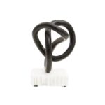 Matte black twisted knot sculpture on a raw-edged white marble base.
