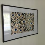 Framed abstract painting with blue and gold eyes on a black background, symbolizing identity and presence.