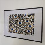 Framed abstract painting with blue and gold eyes on a black background, symbolizing identity and presence.