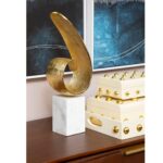 Gold finish curl sculpture on white marble base – modern decorative accent.
