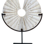 TIBOR Travertine Disc Sculpture featuring a hand-carved circular travertine stone on a sleek black metal base, displayed in a modern living room.