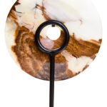Polished round onyx disc in natural earthy tones displayed on a black metal stand.