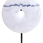 The ZORO Medium White Marble Disc Sculpture features a polished white marble disc with natural veining mounted on a sleek black metal stand, offering a refined and minimalist decorative accent.