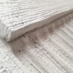 White textured wall art with vertical ribbed detailing and a semi-circular relief in a wooden frame.