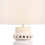 Tall off-white ceramic table lamp with geometric tiered base, circular cut-outs, and a white cylindrical shade.