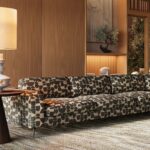 Tall off-white ceramic table lamp with geometric tiered base, circular cut-outs, and a white cylindrical shade.