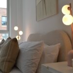 WAVE bed in natural weave fabric with curved upholstered headboard and round wooden legs in neutral modern bedroom.